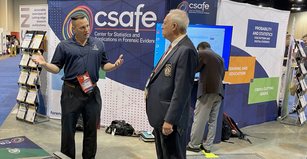 CSAFE researcher Richard Stone, left, talks with a conference attendee about the functions of the footwear scanner device at the CSAFE booth during the 2022 IAI Conference.