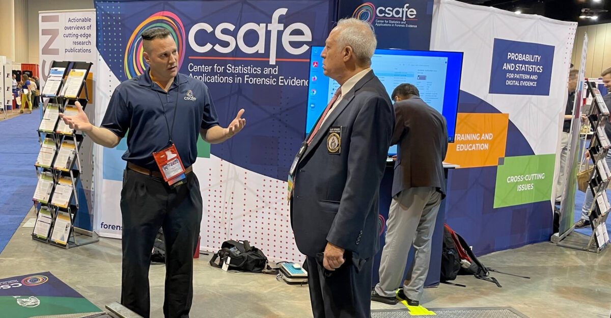 Two men talking at a CSAFE booth at a conference, with displays and banners behind them.