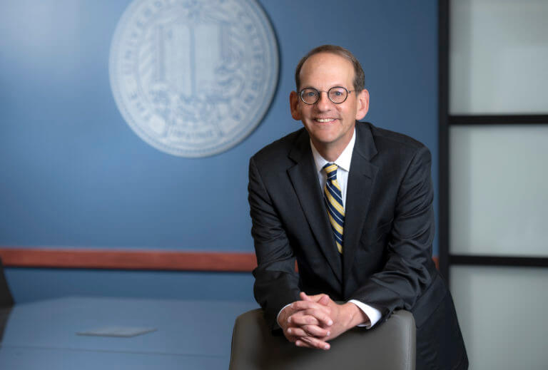 Hal S. Stern leans on a chair in an office with a seal on the wall behind him.