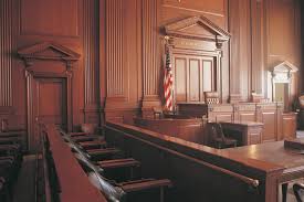 Empty courtroom with wooden benches, judge’s bench, witness stand, and an American flag.