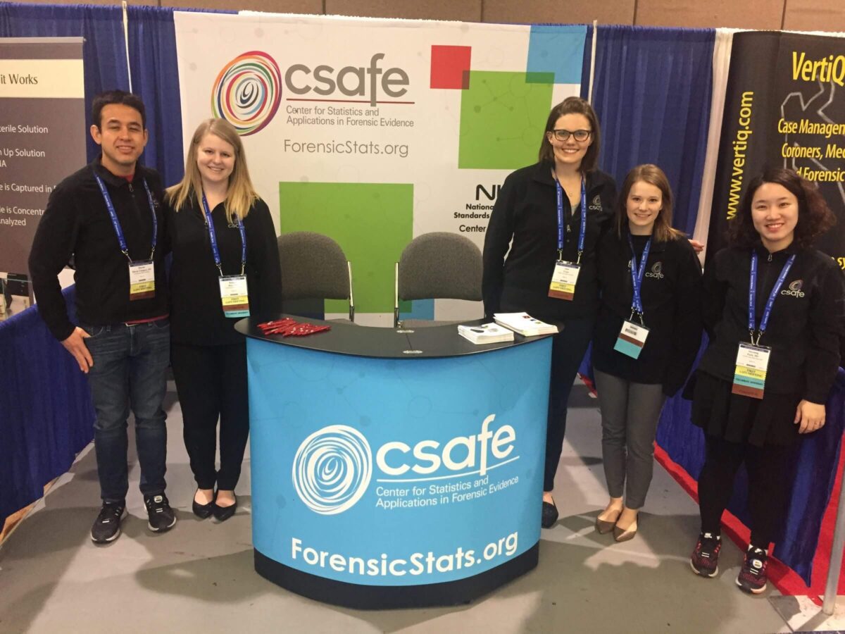 Five people stand smiling at a CSAFE forensic statistics conference booth.