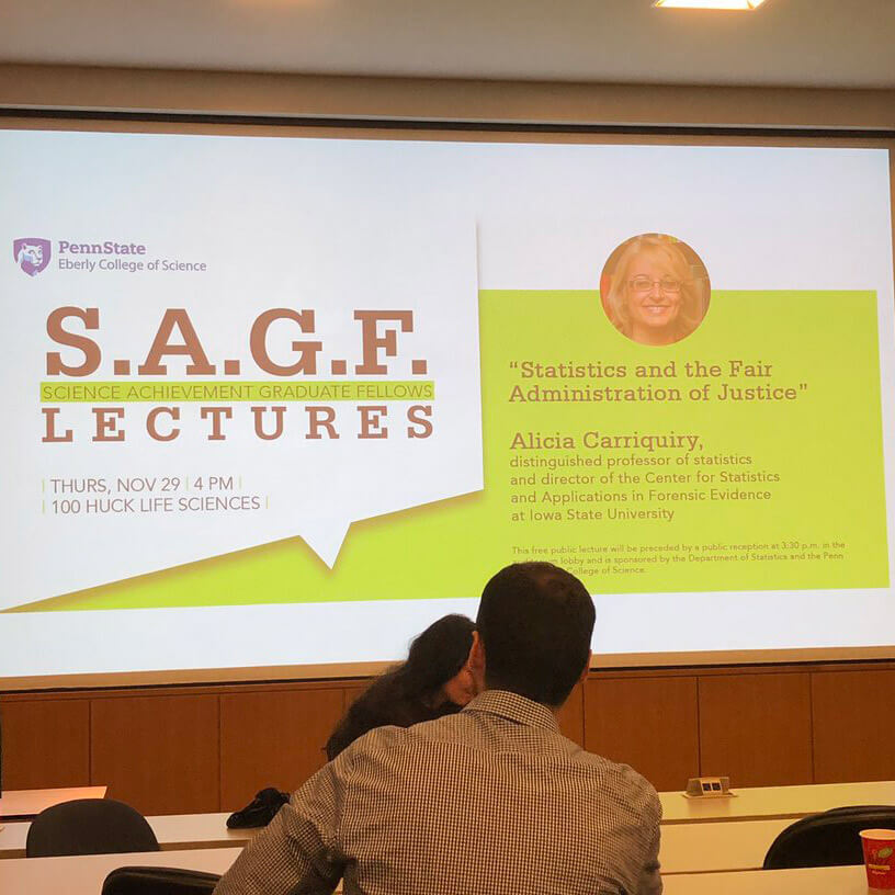 Projector screen showing S.A.G.E. lecture info with Alicia Carriquiry as the speaker.
