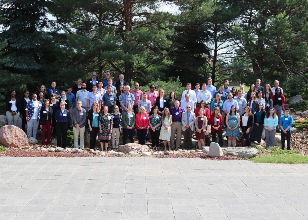 A large group of people pose for a photo outdoors in front of trees and rocks.
