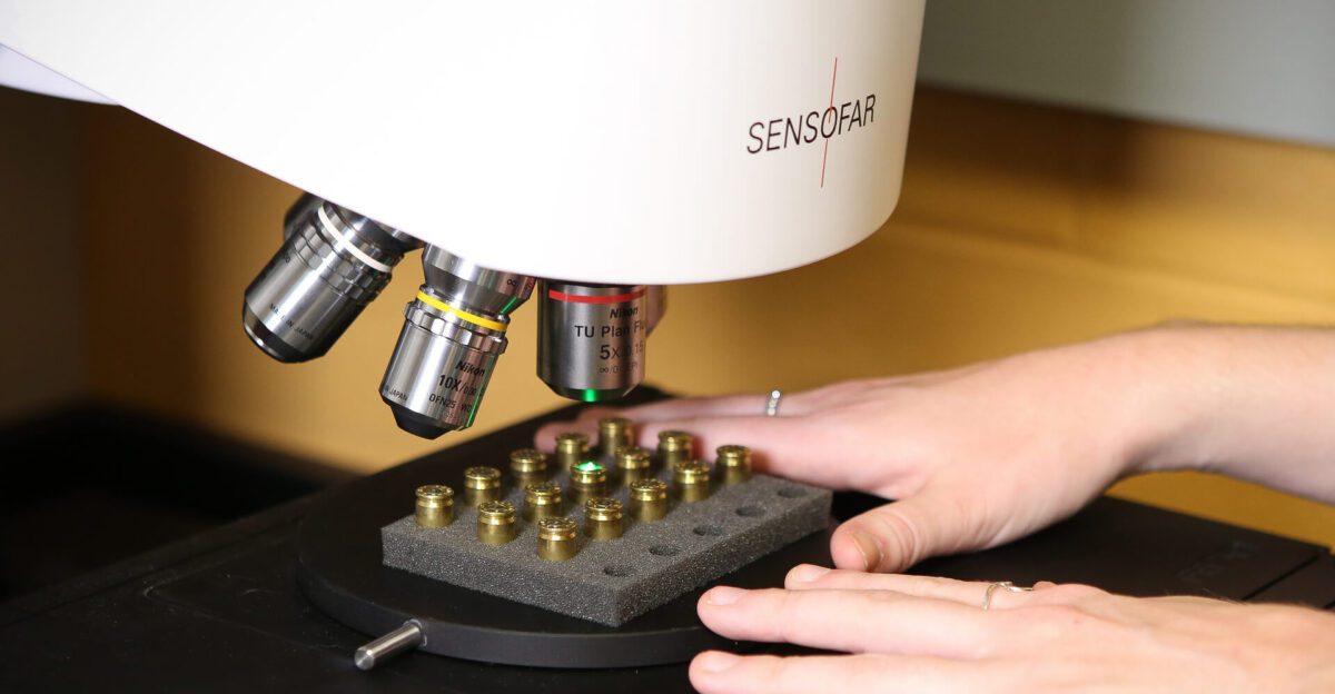 A person places a sample tray under a Sensofar microscope for examination.