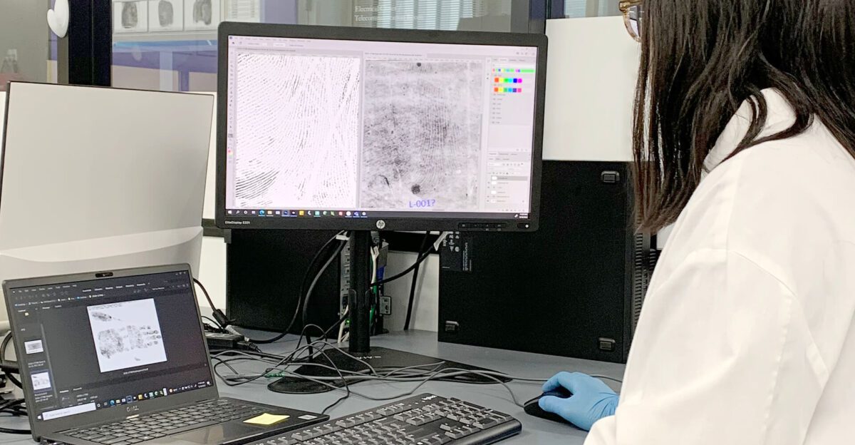 A person analyzes fingerprint images on a computer screen in a laboratory setting.