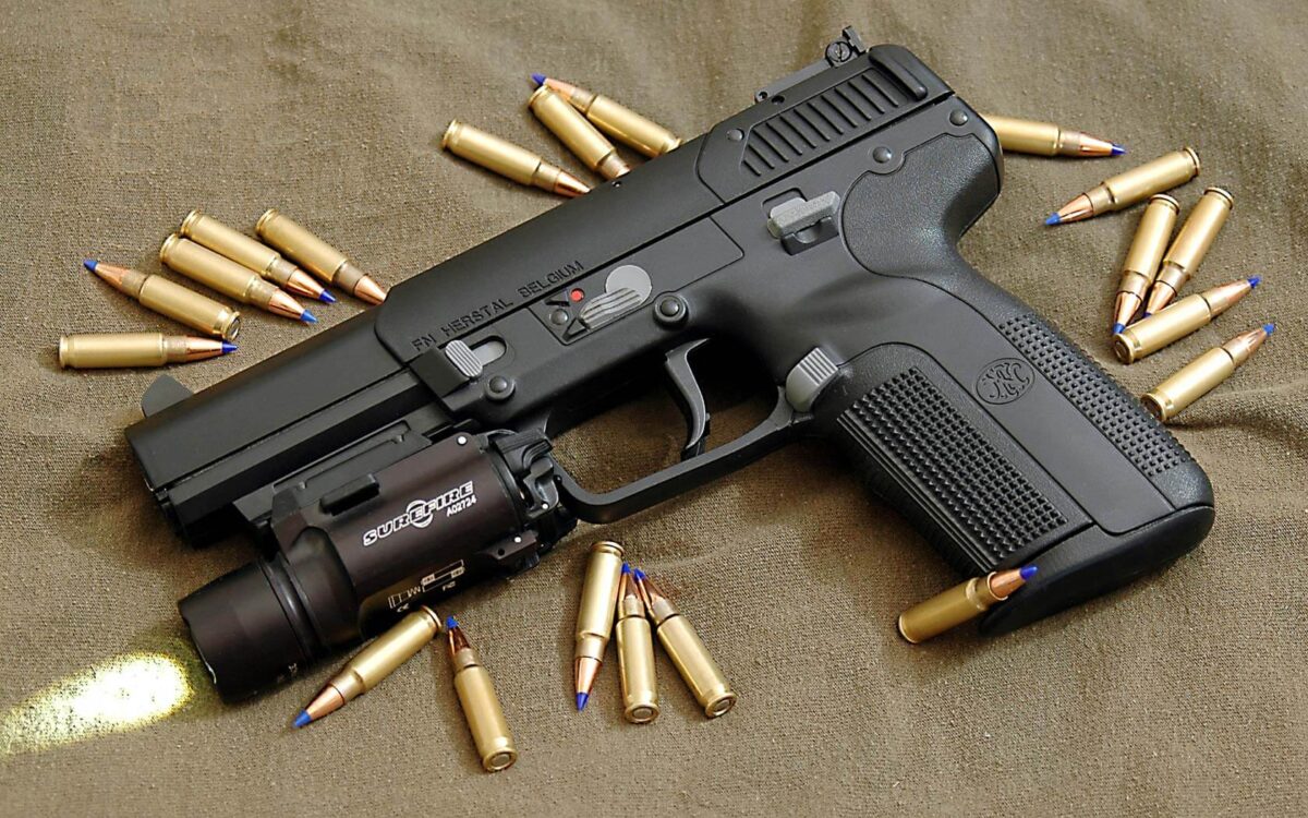 A black handgun with a mounted flashlight, surrounded by scattered bullets on a brown surface.