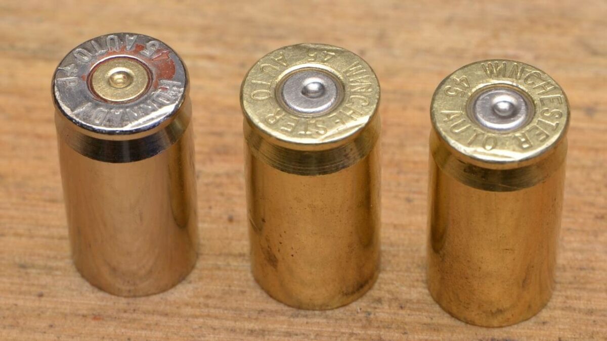 Three .45 caliber brass cartridge casings standing upright on a wooden surface.