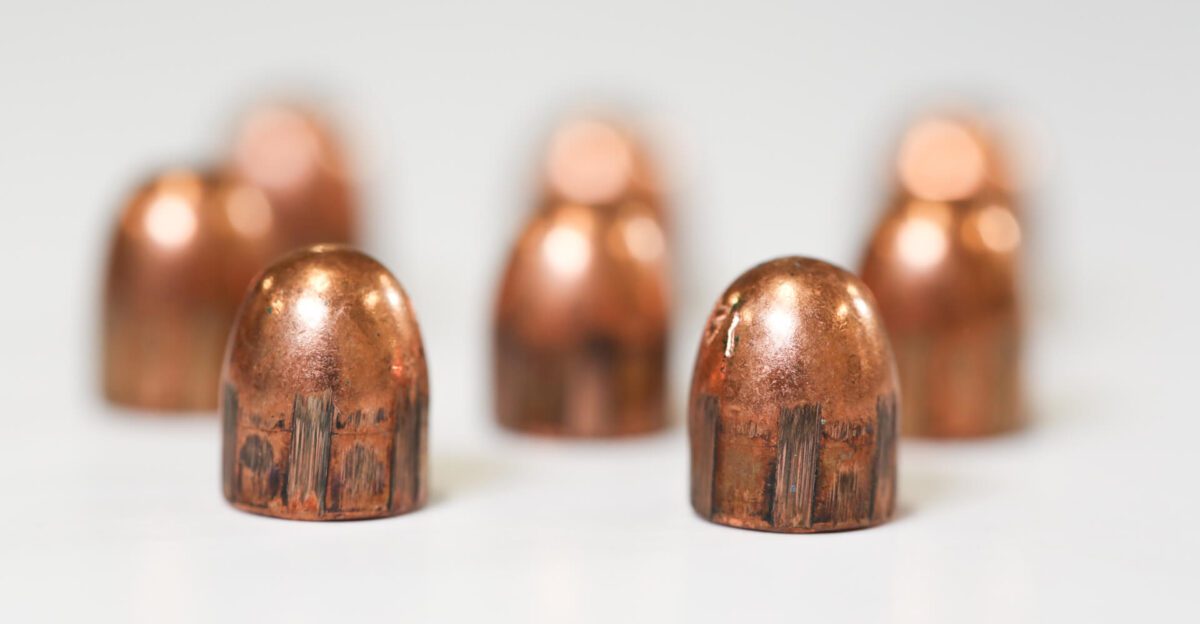 Close-up of seven copper bullets standing upright on a white surface with a blurred background.