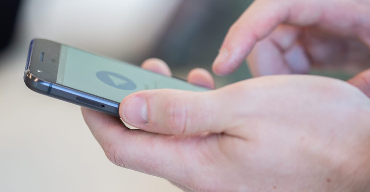 Close-up of hands holding a smartphone, with a finger tapping on the screen.
