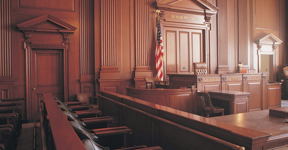 Empty courtroom with wooden benches, judge’s bench, and an American flag.