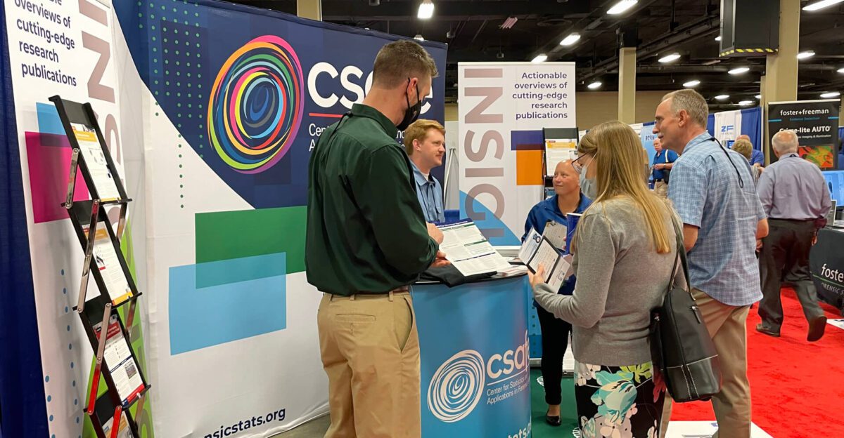 People converse at a colorful research publication booth during a conference or expo event.