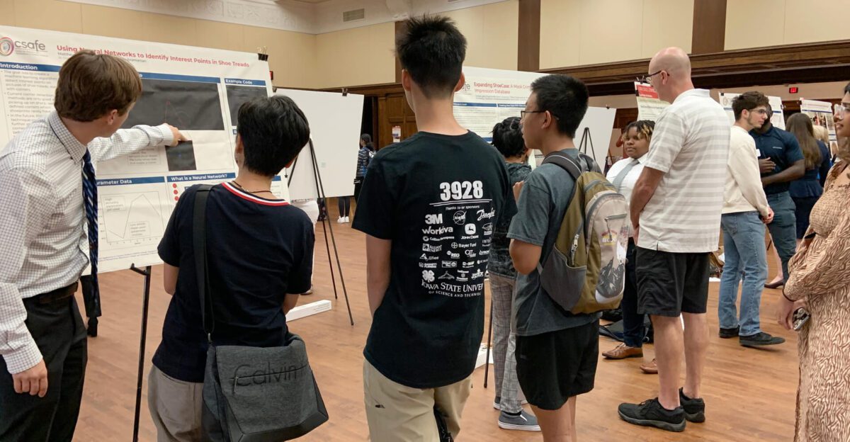 A group of people view and discuss scientific posters at an indoor exhibition or conference.