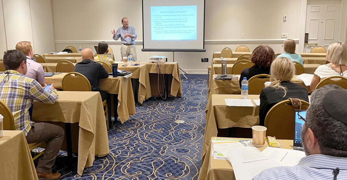 A man gives a presentation to attendees seated at tables in a conference room.