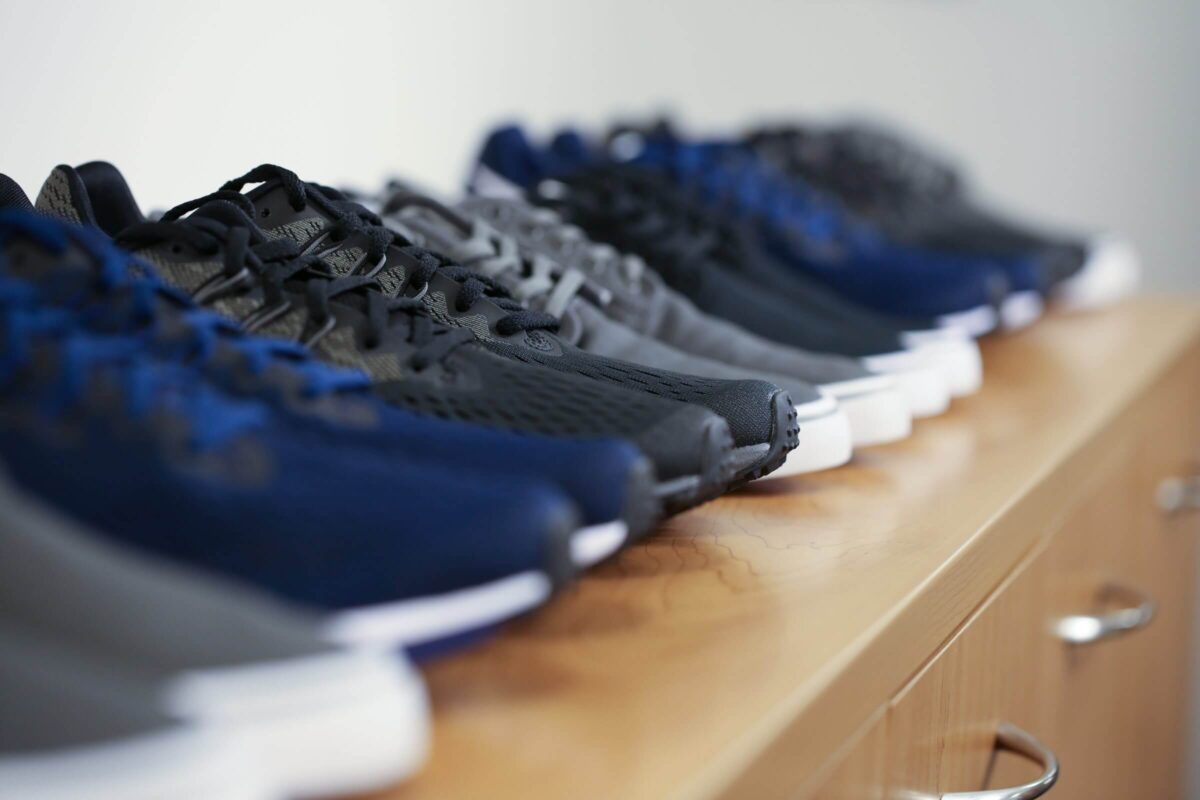 Several pairs of athletic shoes in shades of blue, black, and gray are lined up on a wooden surface.