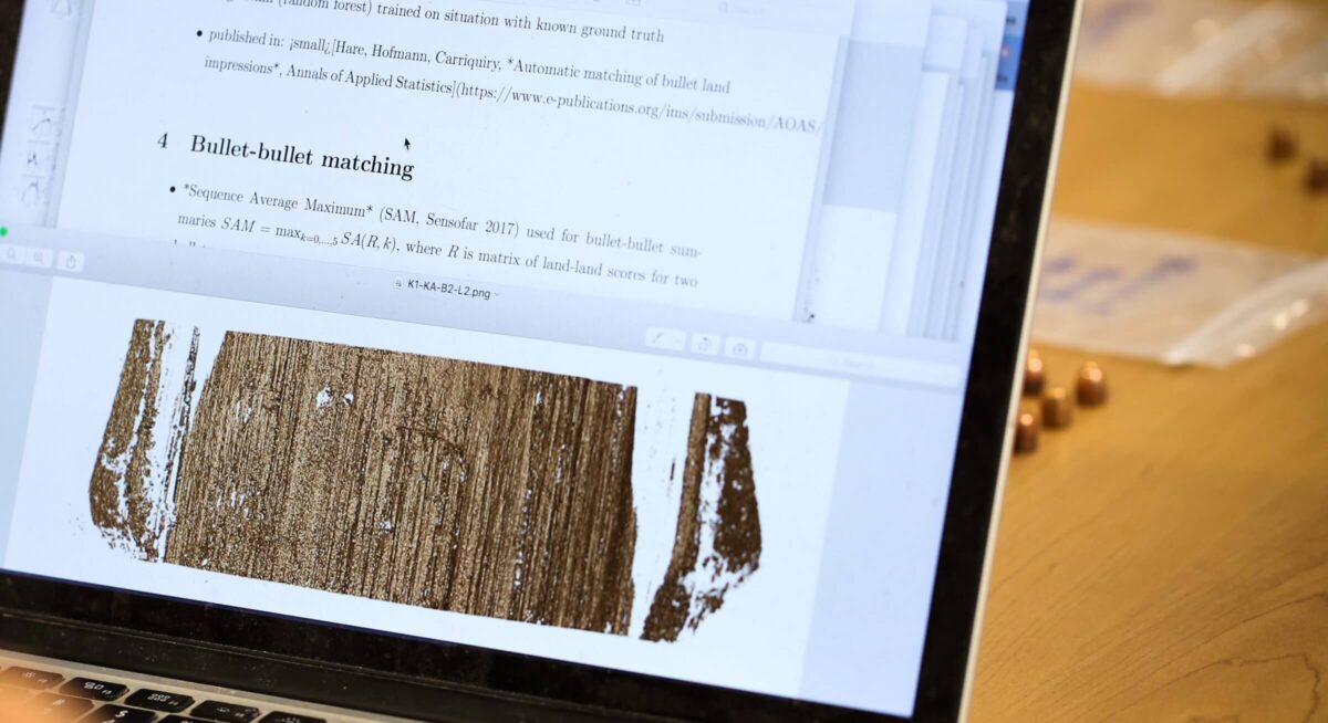 A laptop screen displays a research paper and an image of a marked metal surface.
