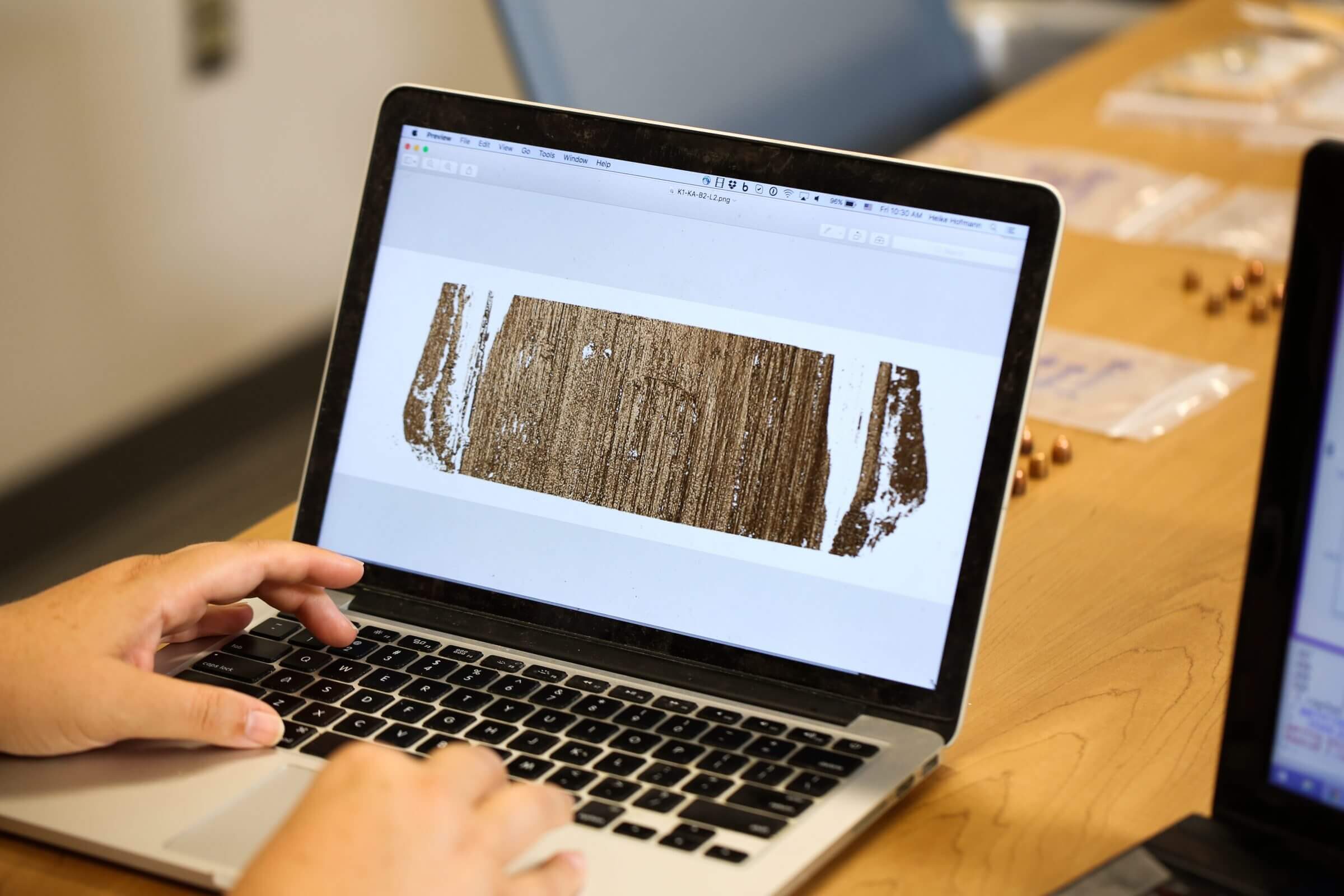 A person examines a scanned image of wood grain on a laptop screen.