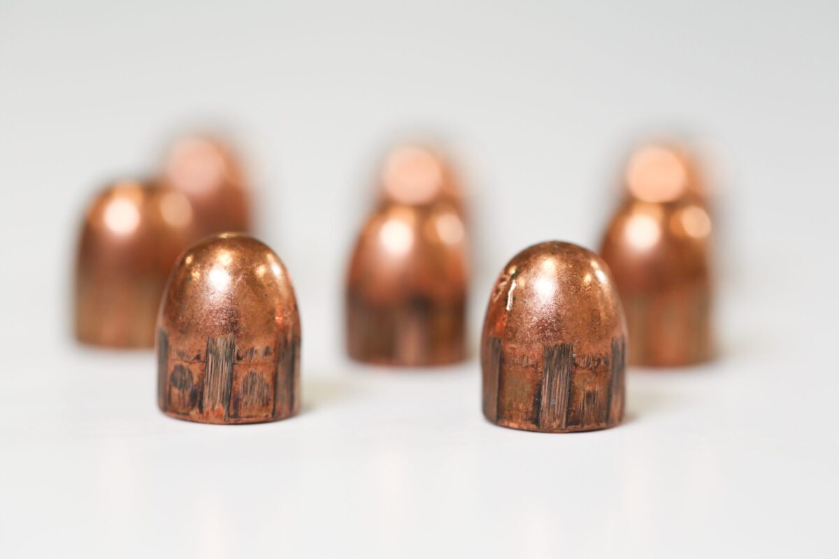 Seven copper bullets are standing upright on a white surface with a soft focus in the background.