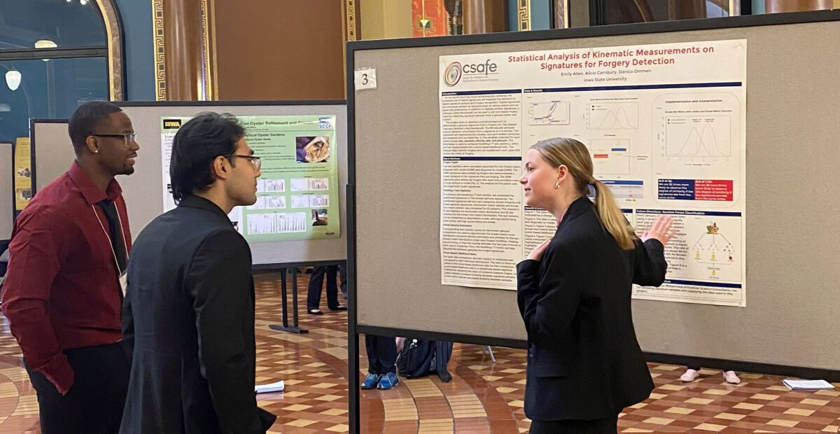 Three people discuss a scientific research poster at an academic conference in a large hall.