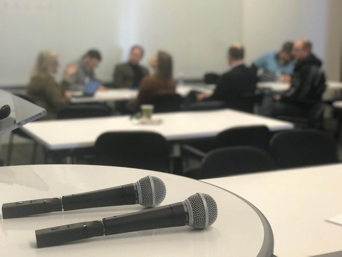 Two microphones on a table with people having a meeting in the background.