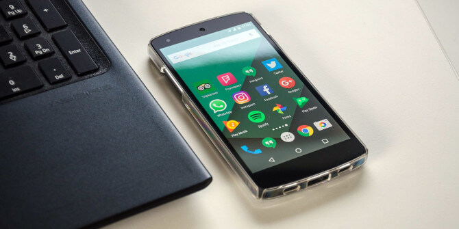 A smartphone with app icons on the screen lies next to a laptop keyboard on a white surface.
