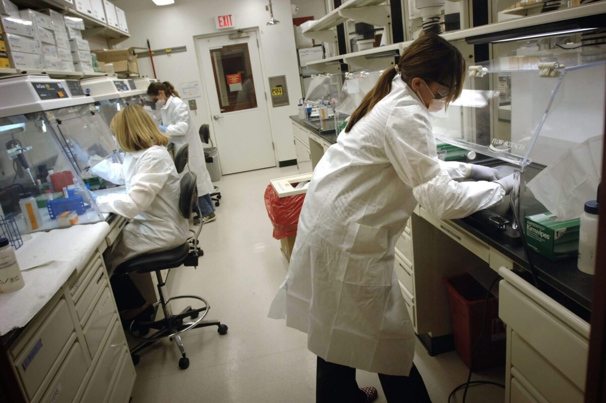 Three scientists in lab coats work at separate lab stations with equipment in a laboratory room.