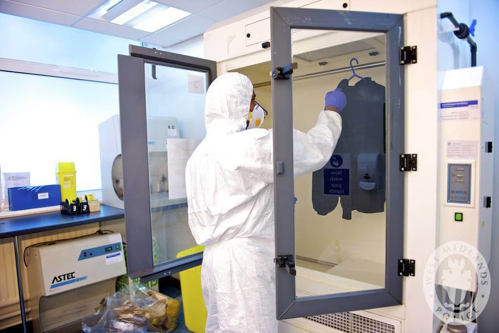 A person in protective gear examines a jacket inside a laboratory fume hood.
