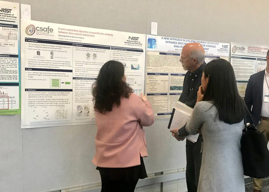 Three people discuss research posters displayed on a conference wall.