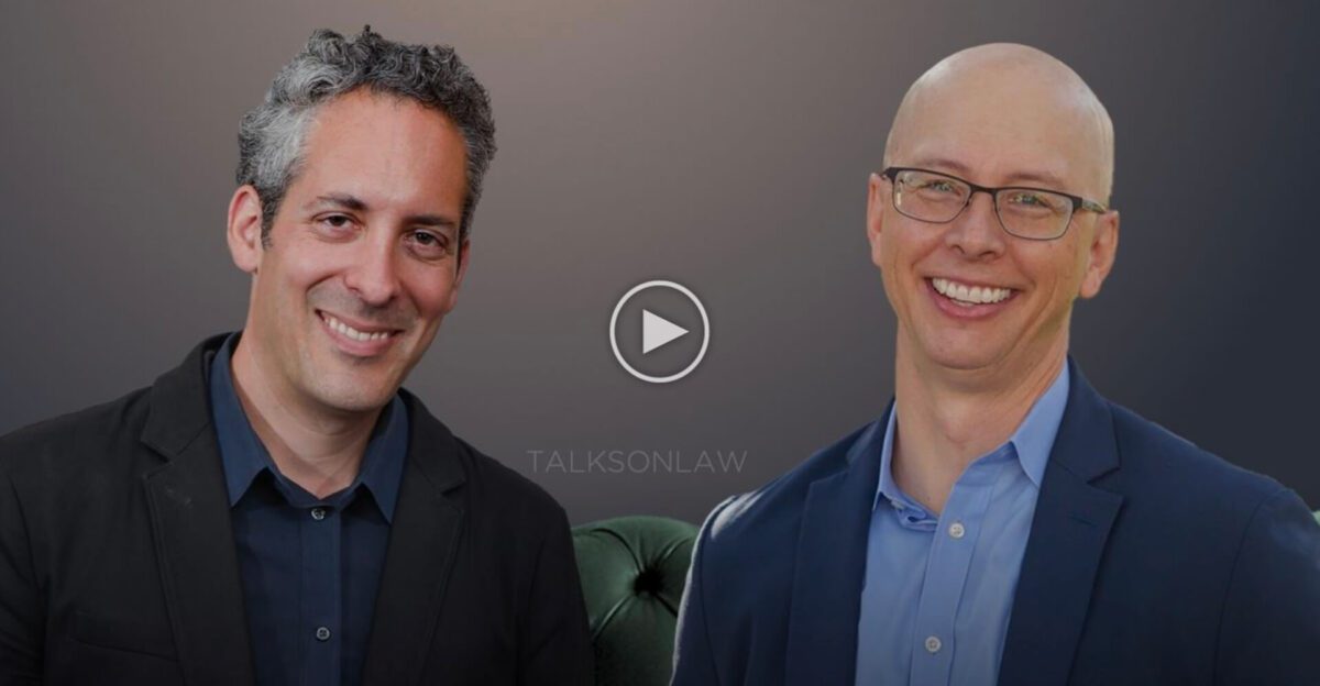 Two men in suits smiling against a dark background with a play button and "TALKSONLAW" text in the center.
