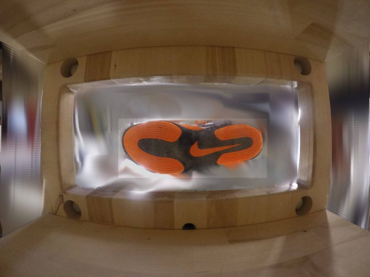View from inside a shoebox, looking up at the orange sole of a Nike sneaker through clear plastic.