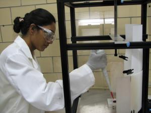 Woman in lab coat and goggles using a pipette in a laboratory setting.