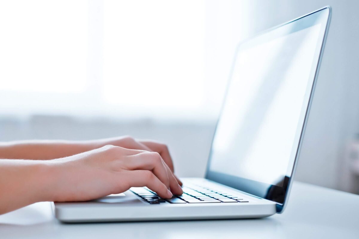 Hands typing on a laptop keyboard, with a bright, blurred background.