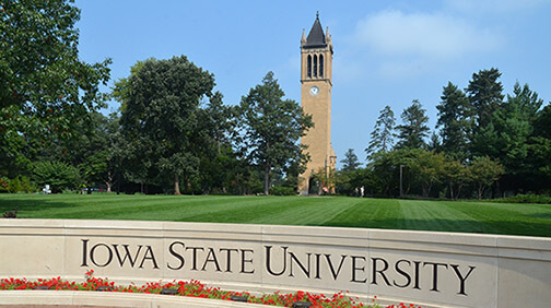 Iowa State University sign with a clock tower and green lawn in the background on a sunny day.