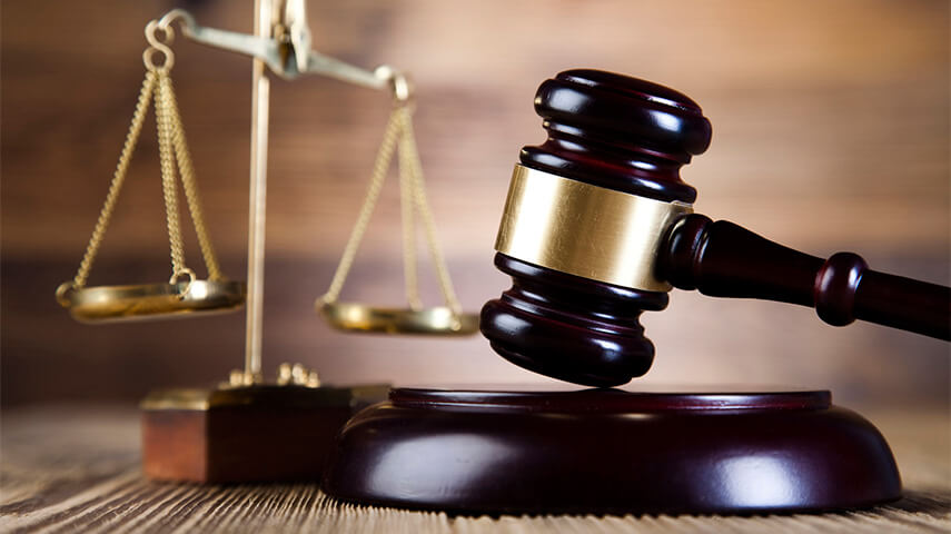 A judge's gavel and a set of brass scales of justice on a wooden table.