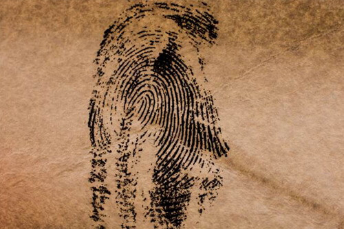 A black fingerprint on brown textured paper, with the print slightly smudged on the left side.