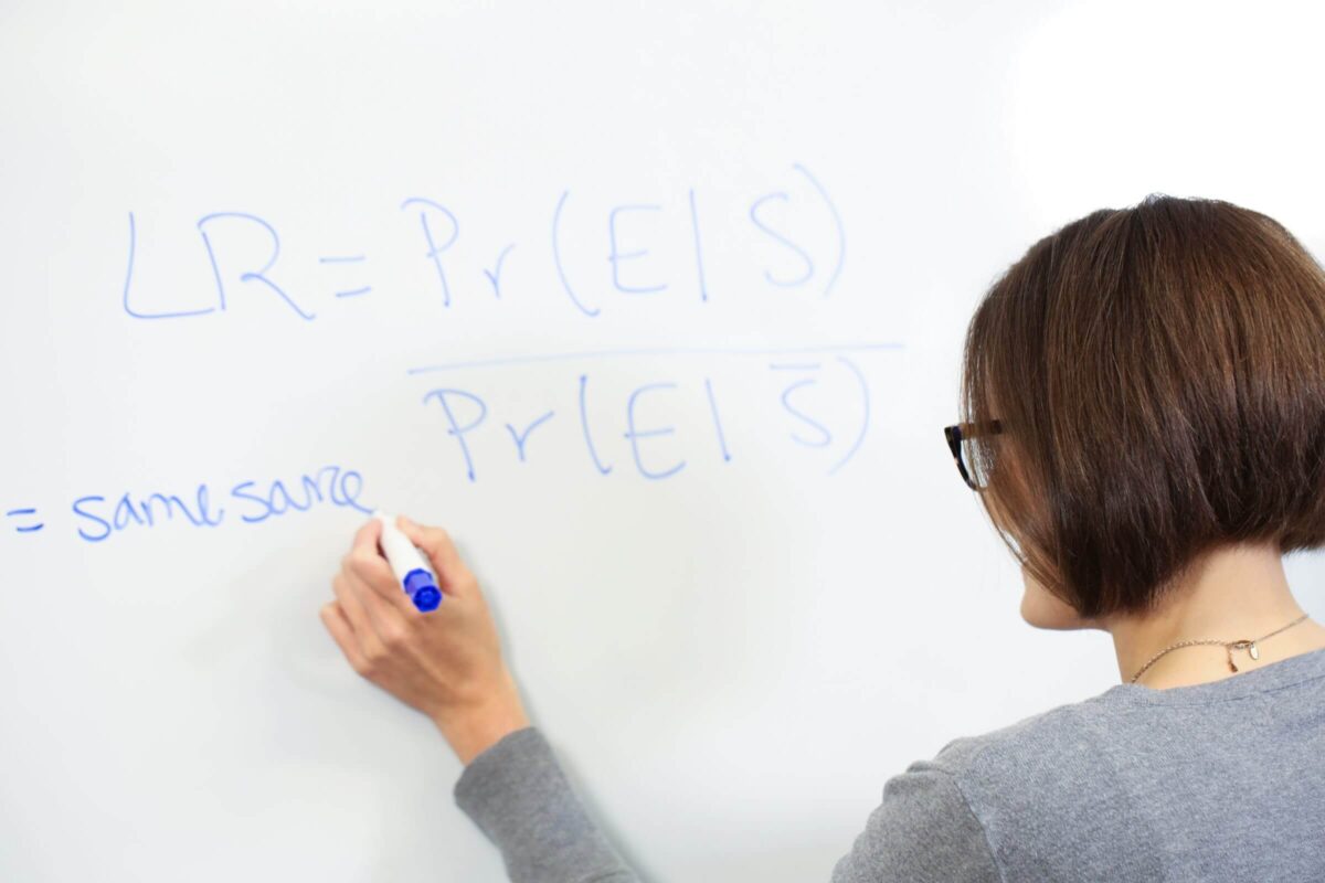 Person writing a probability equation with a blue marker on a whiteboard.