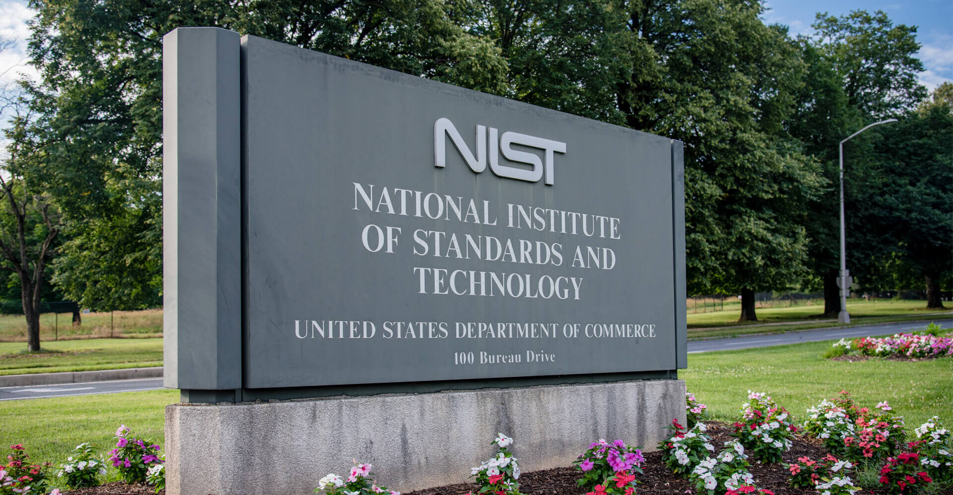 NIST sign outside, surrounded by flowers and trees, on a sunny day.