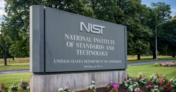 NIST sign outside, surrounded by flowers and trees, on a sunny day.