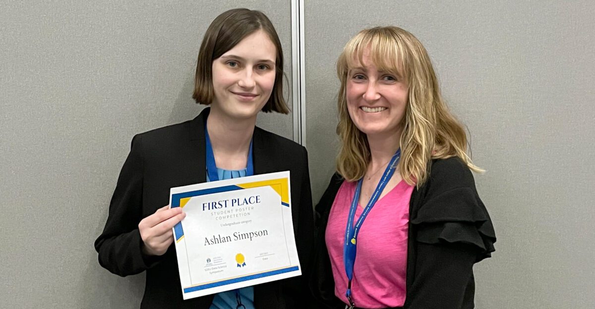 Two women smiling; one is holding a first place certificate that reads "Ashlan Simpson.