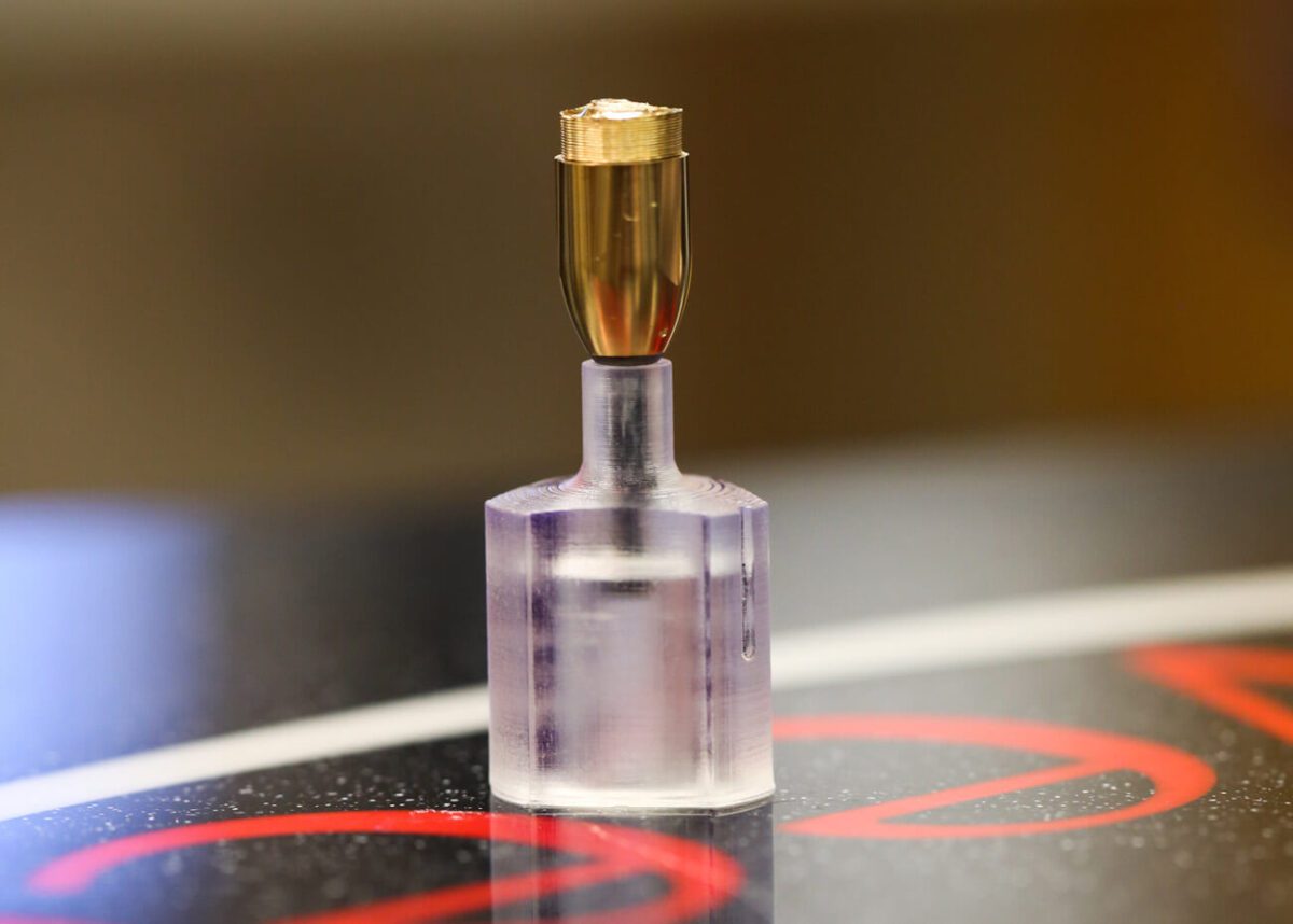 A small metallic object mounted on a clear cylindrical base, placed on a black surface.