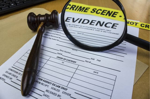 A gavel and magnifying glass on an evidence form with crime scene tape in the background.