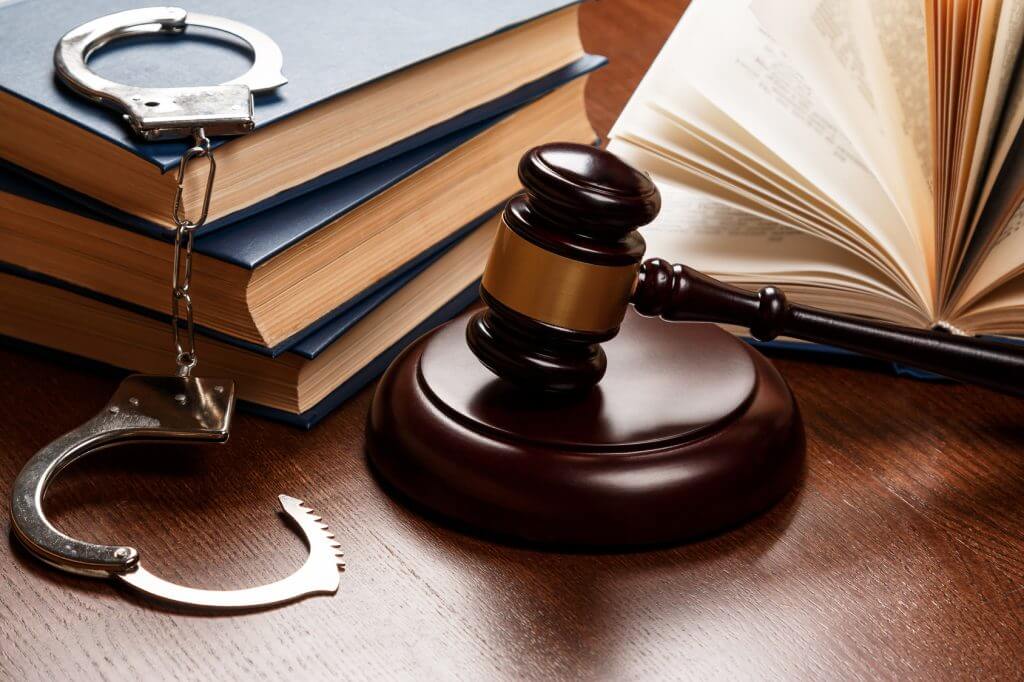 A judge’s gavel, handcuffs, and law books on a wooden desk.